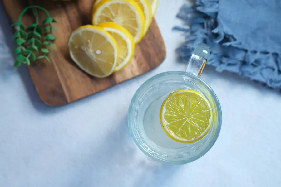 Sliced lemons and a glass of lemon water on a wooden board